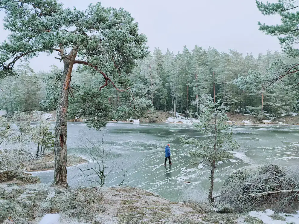 Person walking into a calm, icy lake surrounded by nature