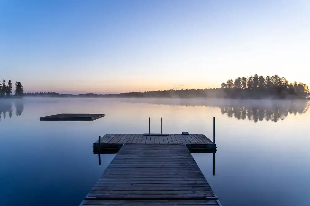 Morning mist over a calm lake near a wooden pier